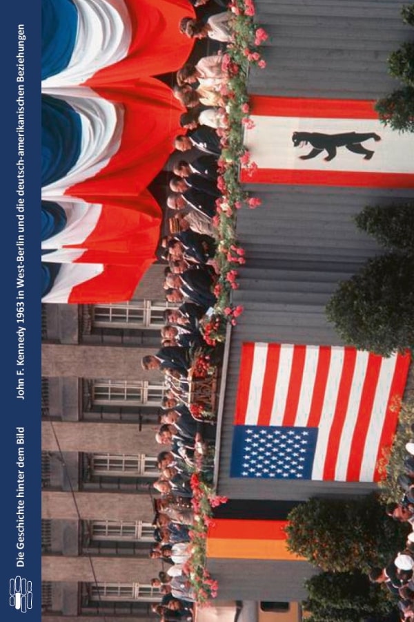 Buchvover "John F. Kennedy 1963 in West-Berlin und die deutsch-amerikanische Beziehungen" von Rolf Steininger. Das Bild zeigt John F. Kennedy bei seiner Rede in Berlin, umgeben von vielen Menschen. Vor ihm hängen die US-Flagge, die Deutschlandflagge und das Berliner Bärenwappen. Er ist umgeben von anderen Menschen