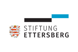 Logo der Stiftung Ettersberg mit einem heraldischen Löwenwappen auf der linken Seite und dem Namen der Stiftung in schwarzer Schrift neben fetten schwarzen und blauen Linien oben rechts.