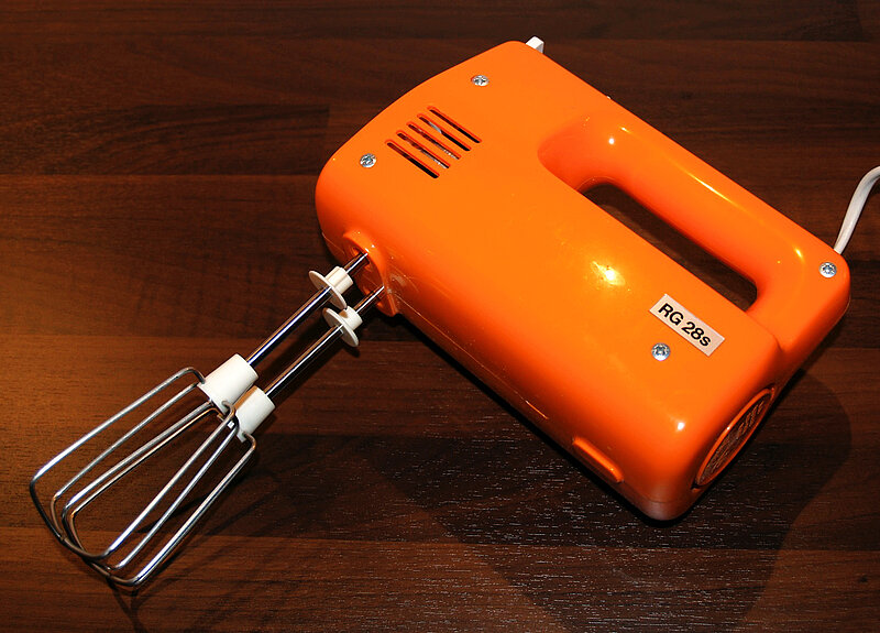 Ein orangefarbenes elektrisches Handrührgerät mit Metallschlägern