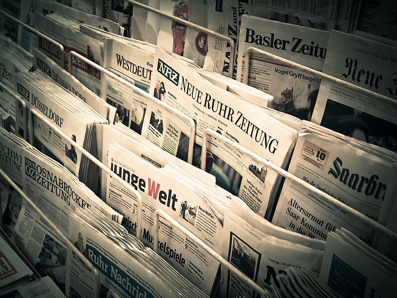 Ein Schaukasten mit verschiedenen deutschsprachigen Zeitungen, die in mehreren Reihen angeordnet sind.