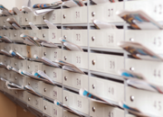 Reihen von Wohnungsbriefkästen mit verschiedenen Poststücken und Zeitschriften, die aus vielen der Schlitze herausragen.