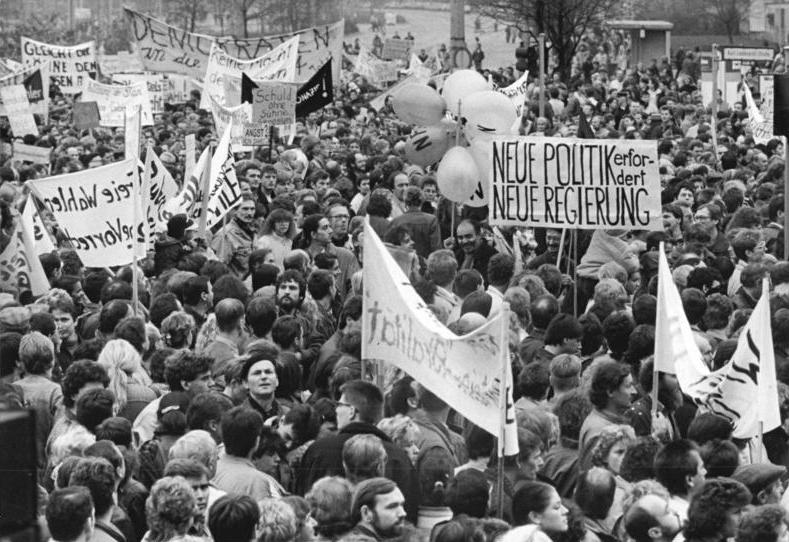 Eine große Menge von Demonstranten mit Schildern und Transparenten versammelt sich im Freien und fordert einen politischen Wandel und eine neue Regierung.