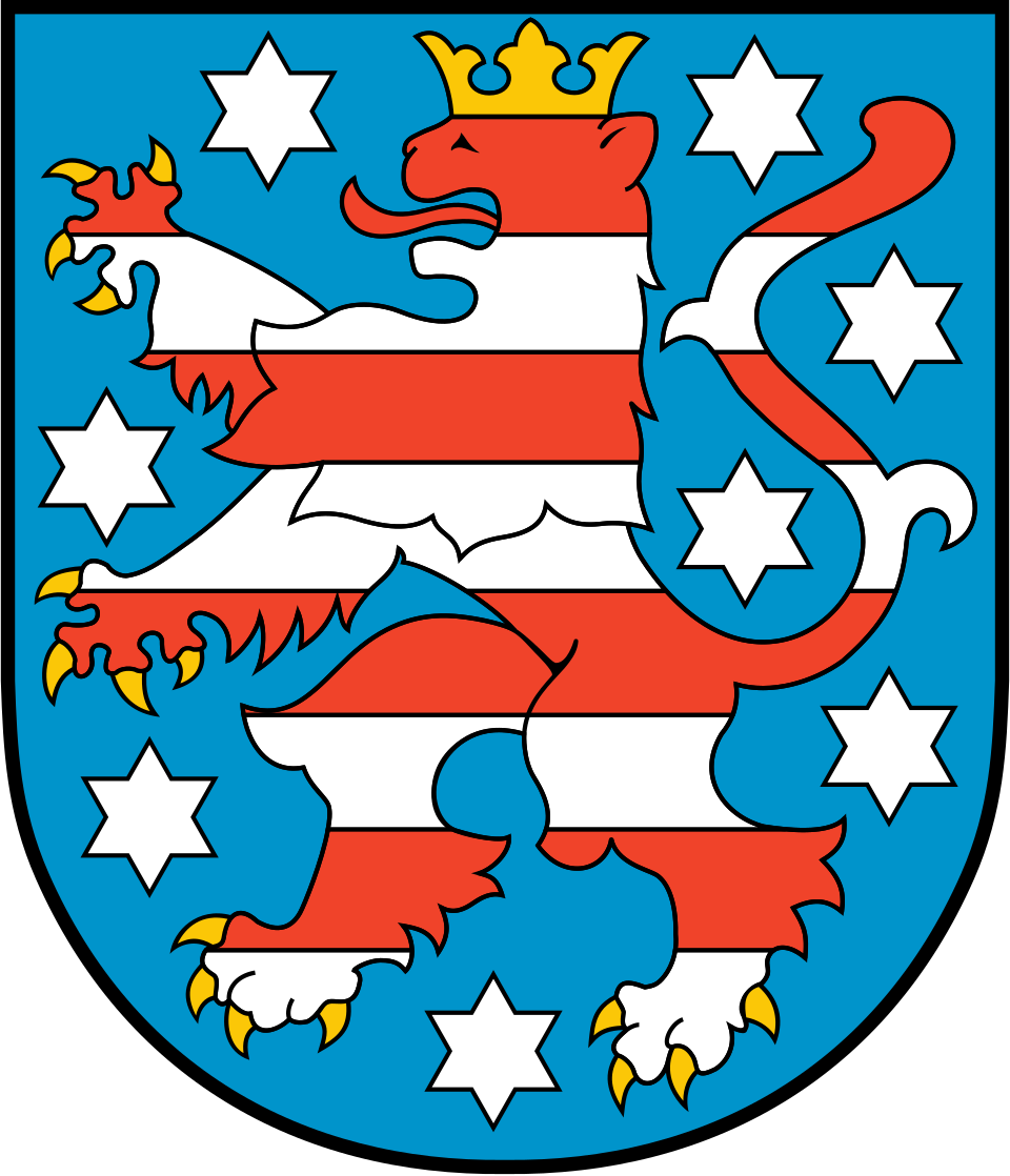 Das Wappen von Thüringen. Es handelt sich um einen weiß-rot gestreiften Löwen mit einer Krone auf einem blauen Hintergrund. Er ist umgeben von acht weißen Sternen