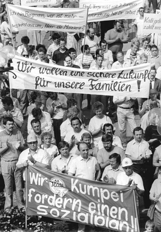 Schwarz-Weiß-Foto einer protestierenden Menschenmenge mit Transparenten, darunter eines mit der Aufschrift "Wir wollen eine sichere Zukunft für unsere Familien" und eines mit "Wir Kumpel fordern einen Sozialplan"..