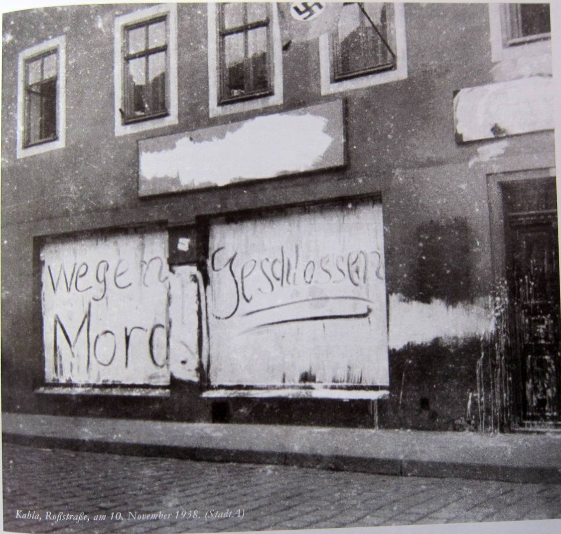 Schwarz-Weiß-Foto eines Gebäudes mit vernagelten Fenstern und Graffiti mit der Aufschrift "wegen Mord geschlossen" in einer Straße; aufgenommen im November 1938.