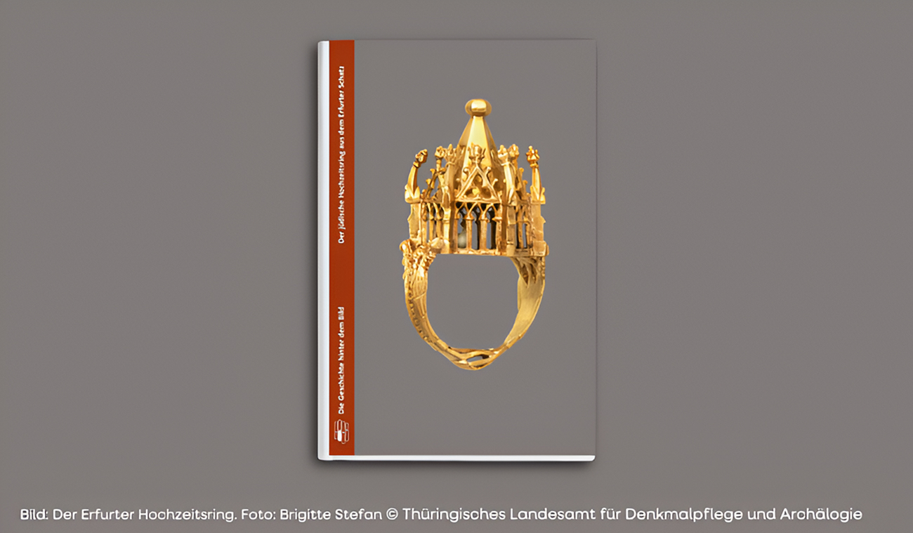 Ein Buch mit einem grauen Einband, auf dem ein goldener mittelalterlicher Ring mit verschlungenen architektonischen Mustern abgebildet ist, steht vor einem grauen Hintergrund.