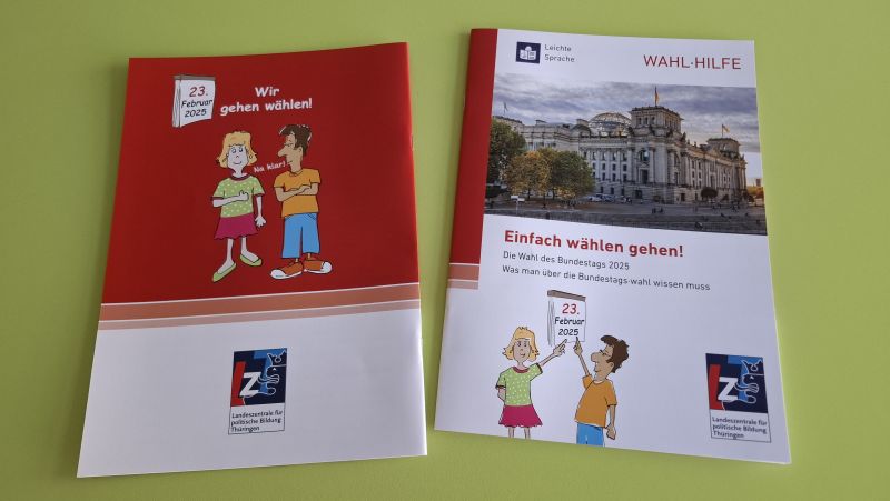 Auf einer grünen Fläche liegen zwei deutsche Wahlbroschüren aus, eine mit Cartoon-Figuren, die andere zeigt das Reichstagsgebäude. Beide sind für die Bundestagswahl 2025 in einfacher Sprache.