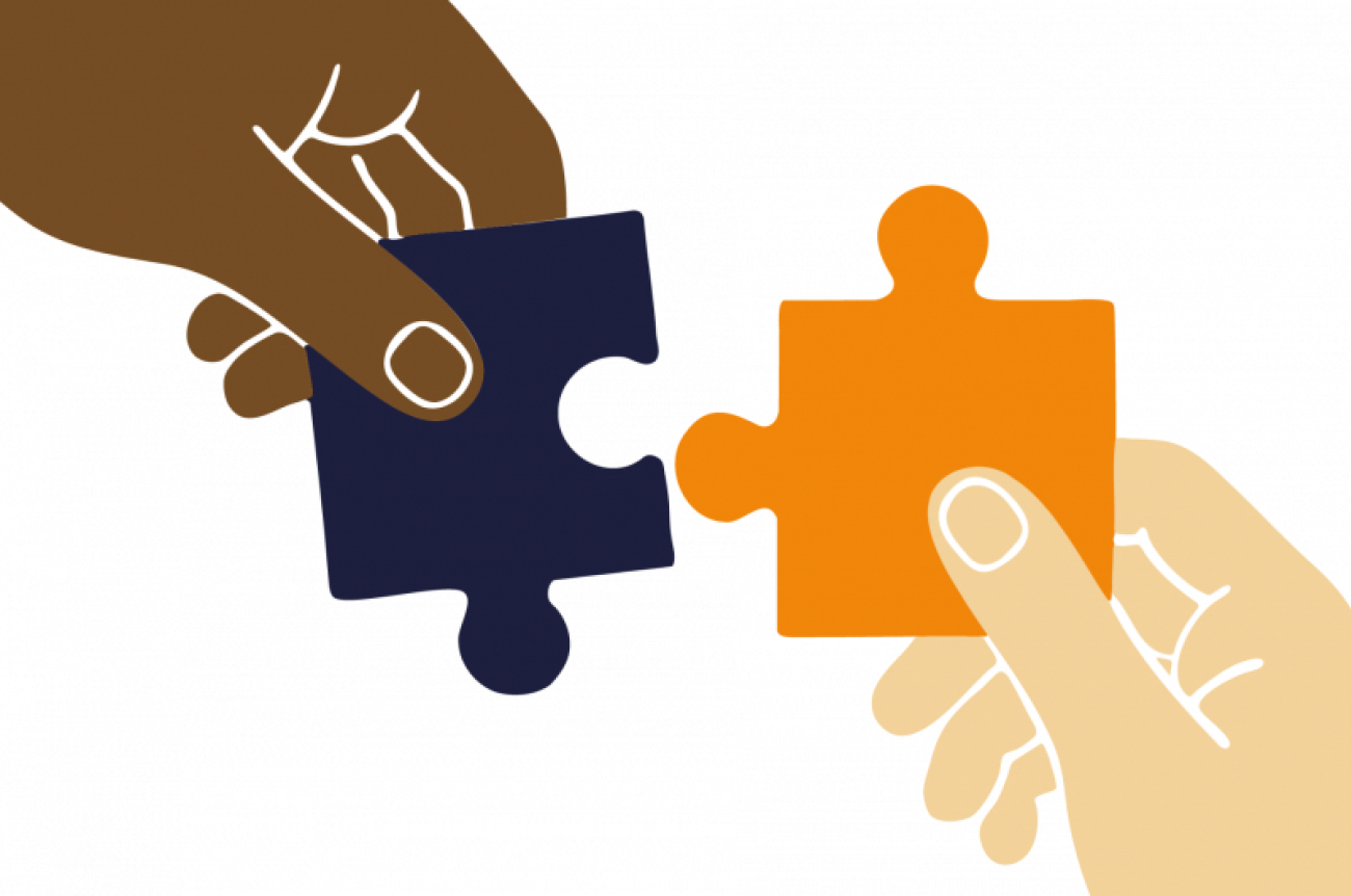 Zwei Hände, eine dunkelhäutige und eine hellhäutige, die jeweils ein Puzzleteil halten, sind dabei zu sehen, wie sie die Teile zusammenfügen.