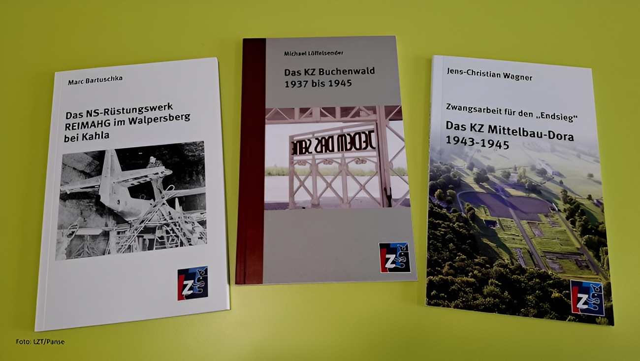 Drei deutschsprachige Bücher über Konzentrations- und Zwangsarbeitslager der Nazis sind auf einer gelben Fläche ausgestellt. Jedes Buch hat ein Foto auf dem vorderen Einband.