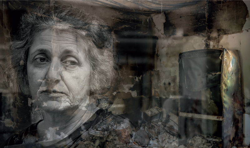 Ein Graustufenbild zeigt eine Frau mit düsterem Gesichtsausdruck vor einem beschädigten, unordentlichen Innenraum mit abblätternden Wänden und Trümmern.