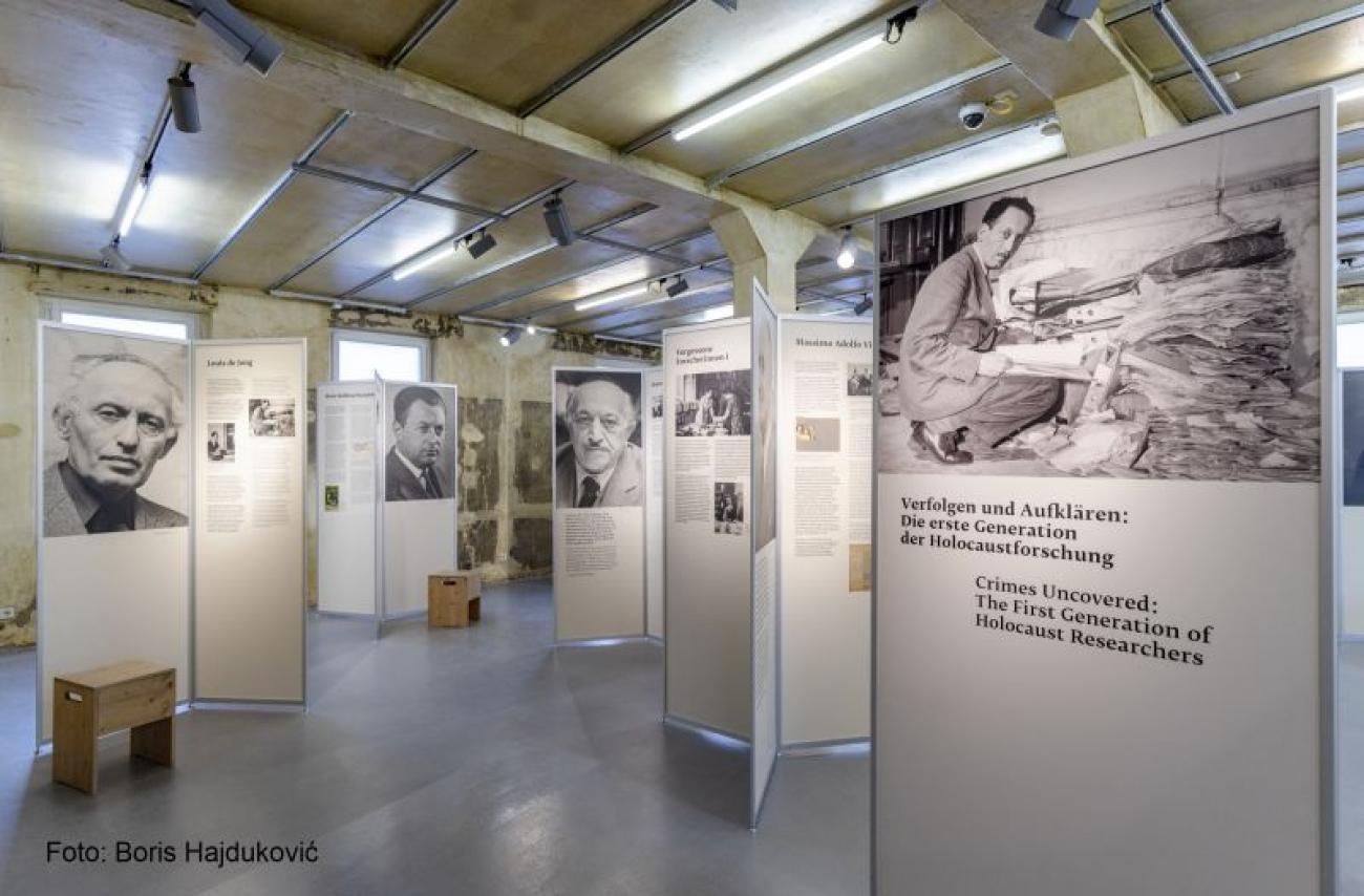 Ausstellungsraum des Museums mit großen Schautafeln mit Fotos und Texten über Holocaust-Forscher; Decke im Industriestil und Leuchten darüber.
